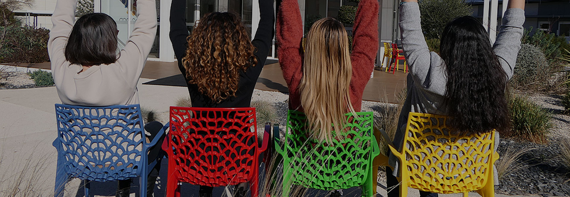 Four people sitting on colourful chairs and raising their hands. Viewed from the back. (photo)
