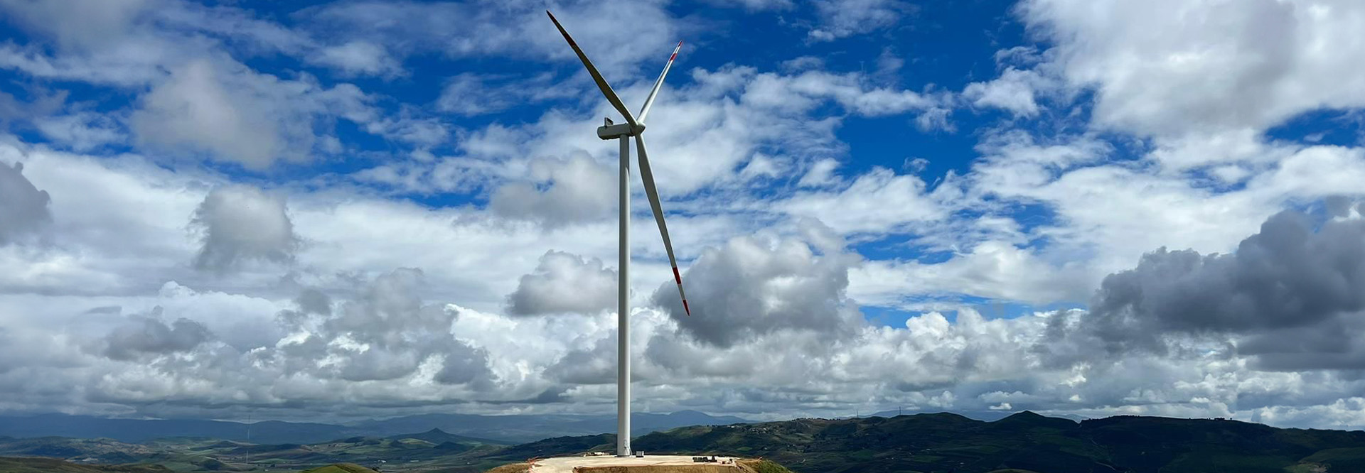 A wind turbine. Mountains and clouds in the background (photo)